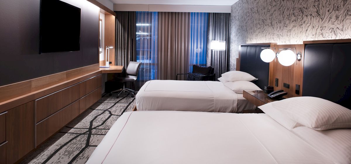 A modern hotel room with two neatly made beds, dark headboards, and curtains beside large windows.