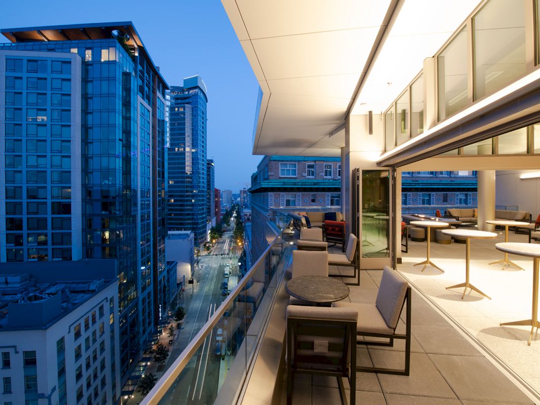 Modern balcony lounge with seating overlooks city streets and skyscrapers at dusk.