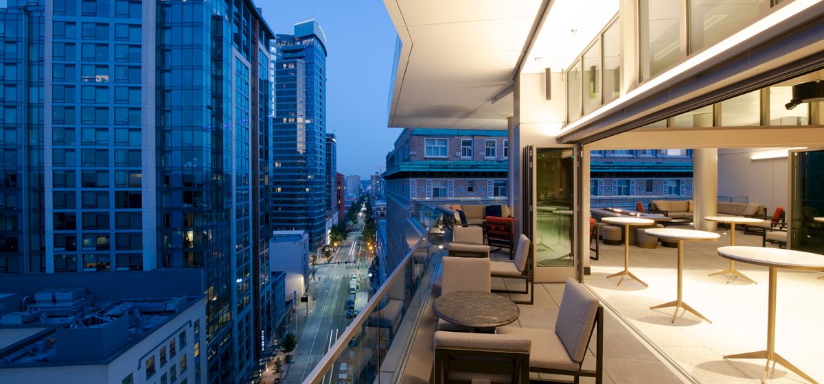 Modern balcony lounge with seating overlooks city streets and skyscrapers at dusk.